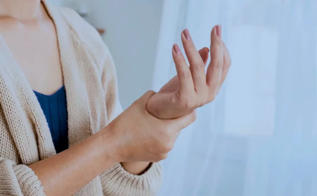 Mujer que se pregunta “¿por qué me duelen las articulaciones con el frío?” mientras se aprieta con la mano la otra muñeca.