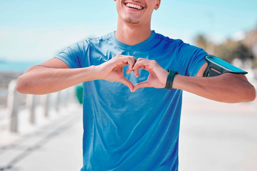 Hombre con ropa de corredor haciendo el símbolo de un corazón con las manos para representar recuperación tras un infarto agudo de miocardio.