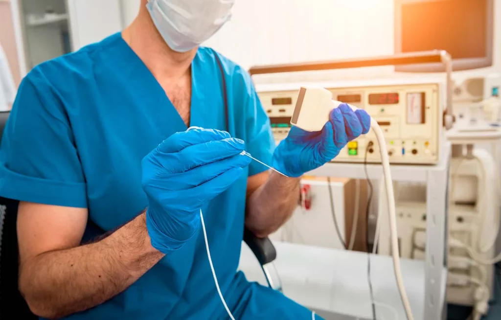  Para procedimiento de cardiología intervencionista, un médico está sentado mientras prepara el equipo que utiliza, incluyendo una aguja y ultrasonido.