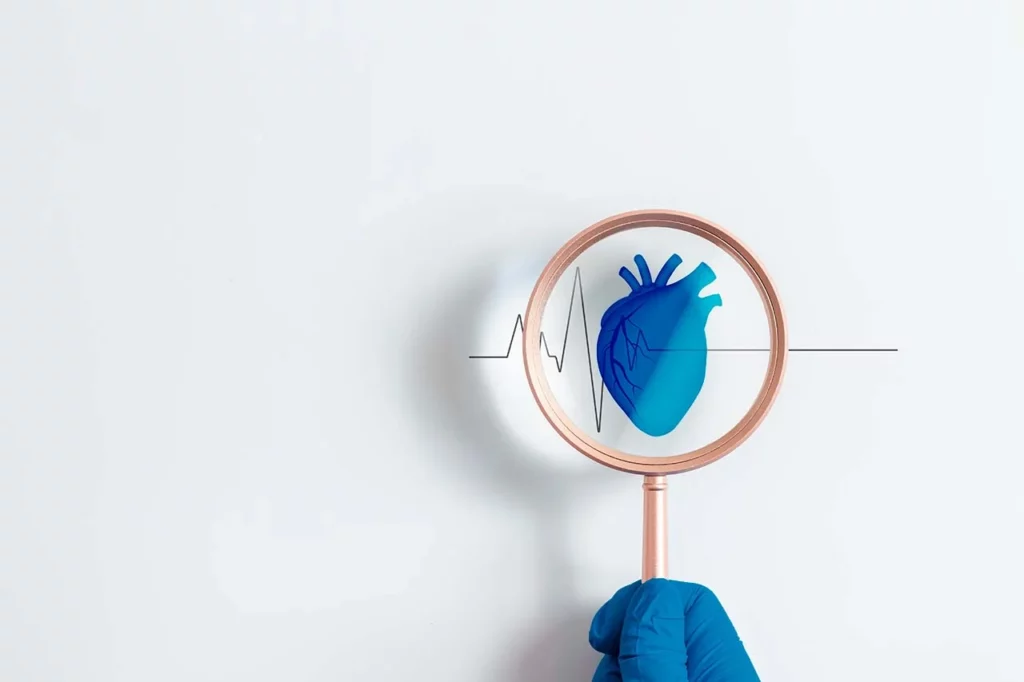 Dibujo de un corazón y unas ondas de electrocardiograma, con una mano sosteniendo una lupa para representar a la cardiología clínica.
