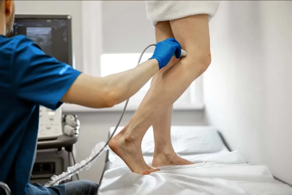 Médico angiólogo realizando un ultrasonido del sistema vascular en las piernas de una paciente.