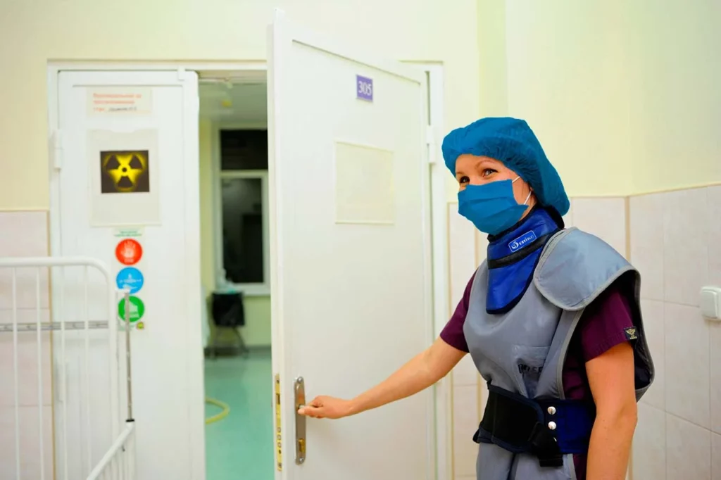 Especialista en cardiología nuclear, parada frente a una puerta con un símbolo de radioactividad, que lleva al área de medicina nuclear en el hospital.