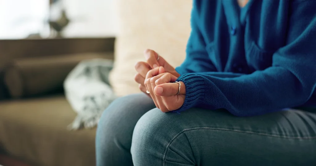 Mujer con ansiedad, sentada en un sillón, con los puños cerrados, mientras identifica los síntomas que está presentando.