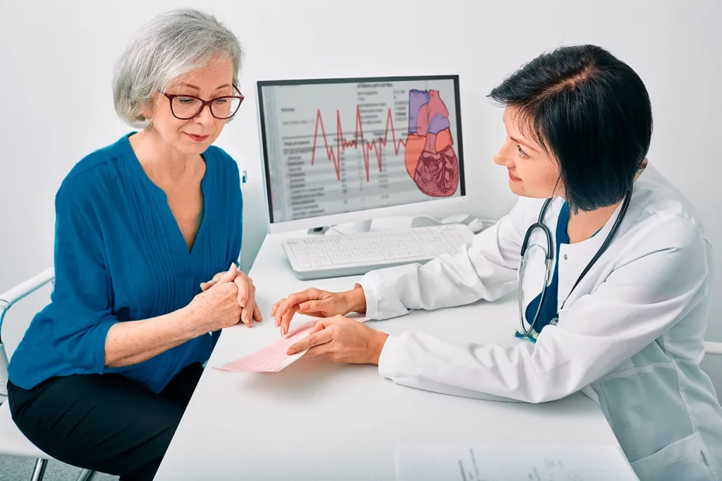 Doctora muestra resultados del estudio para identificar la arritmia que tiene a su paciente mujer, quien los revisa con la mirada.