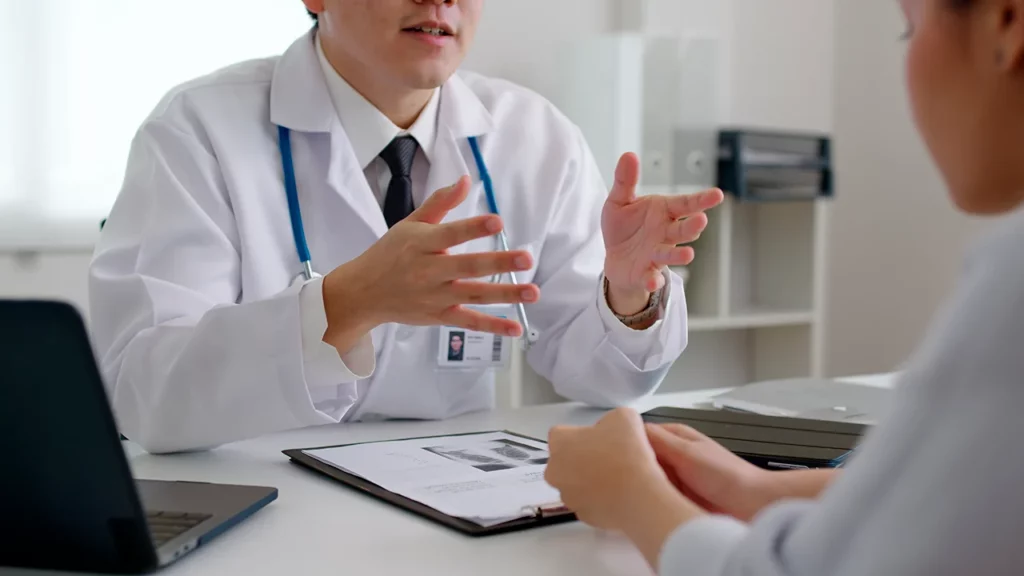 Médico en consulta, explicando los síntomas de cáncer y sus opciones de tratamiento a un paciente.