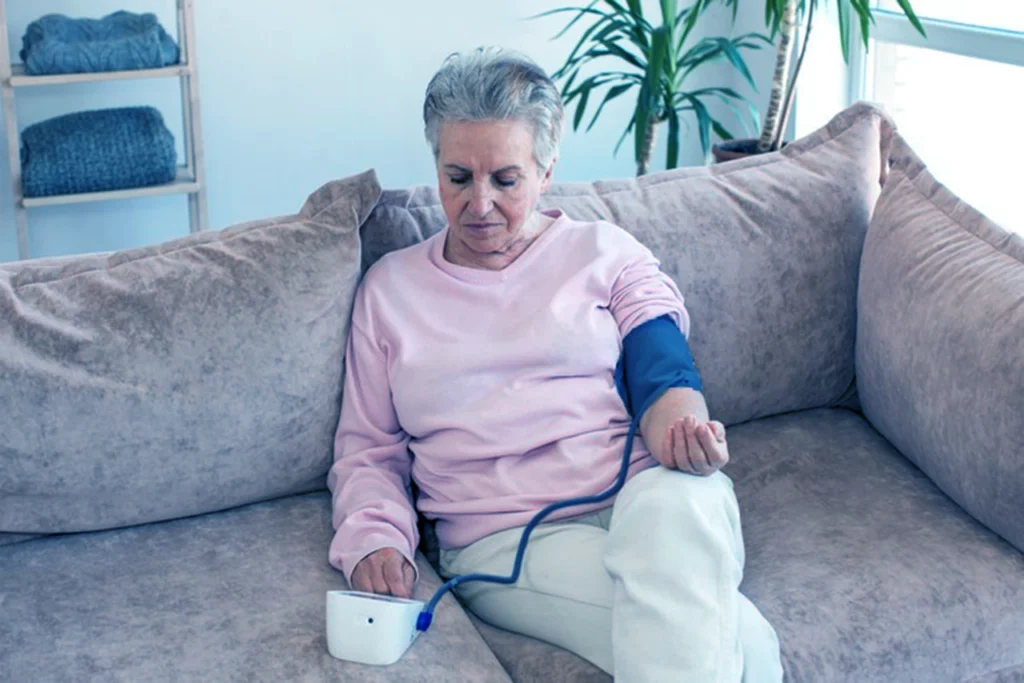 Mujer con cardiopatía hipertensiva midiéndose la presión en el brazo con un equipo automático.