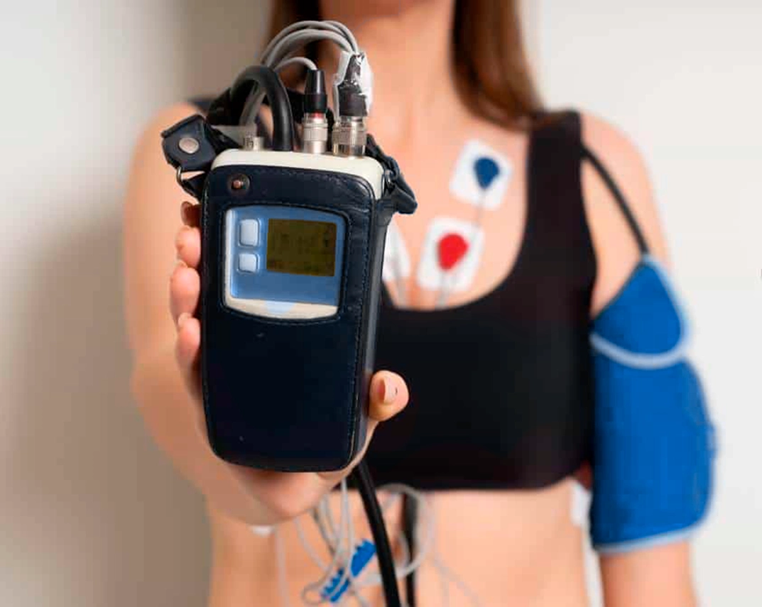 Joven con monitor cardio realizando un estudio del trabajo del corazón en la Clínica de Arritmias, con monitor Holter y sensores de ECG para diagnóstico médico, medición de la presión arterial y evaluación en cardiología.