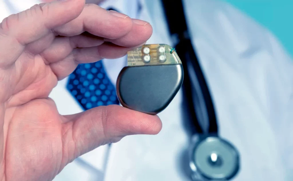 Médico indicando para qué sirve el marcapasos, mientras sostiene el dispositivo entre sus dedos.