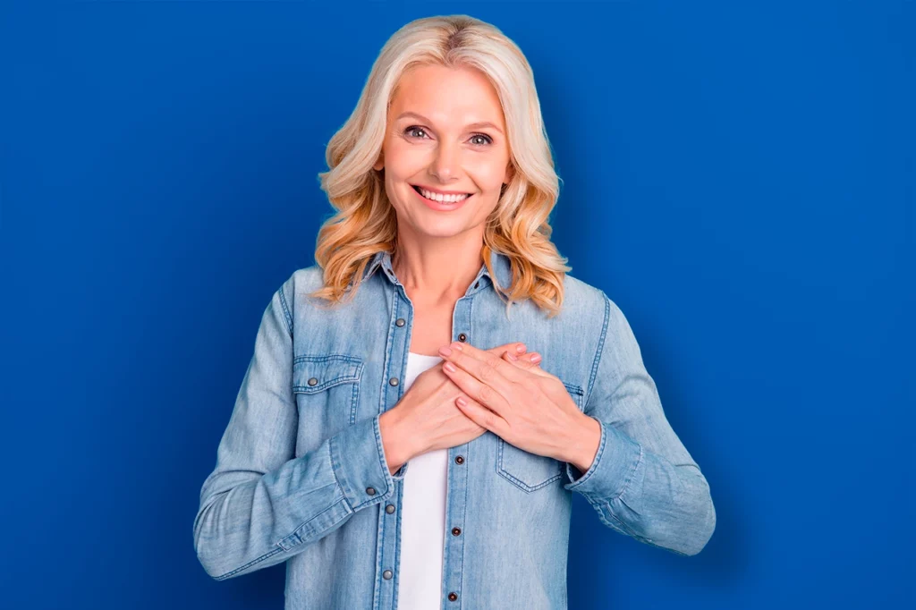 Mujer sin riesgo cardiovascular, se encuentra de pie y con las manos al nivel del corazón mientras sonríe.