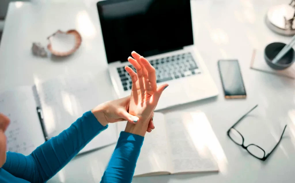 Mujer apretándose la muñeca a causa del dolor de la tendinitis de mano y el celular.