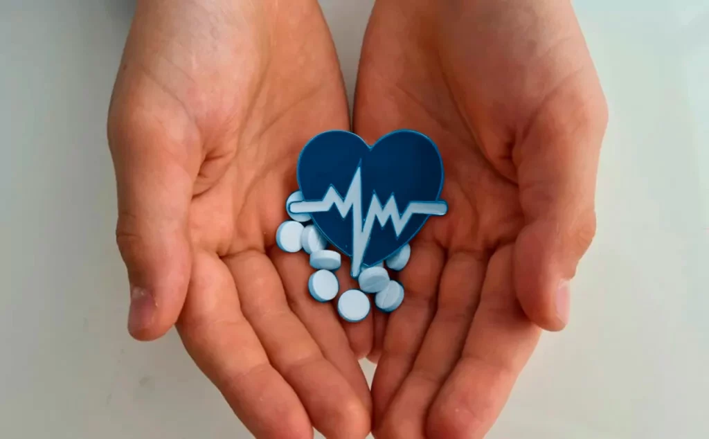 Manos de una persona sosteniendo una figura de corazón y pastillas, para representar las enfermedades del corazón.