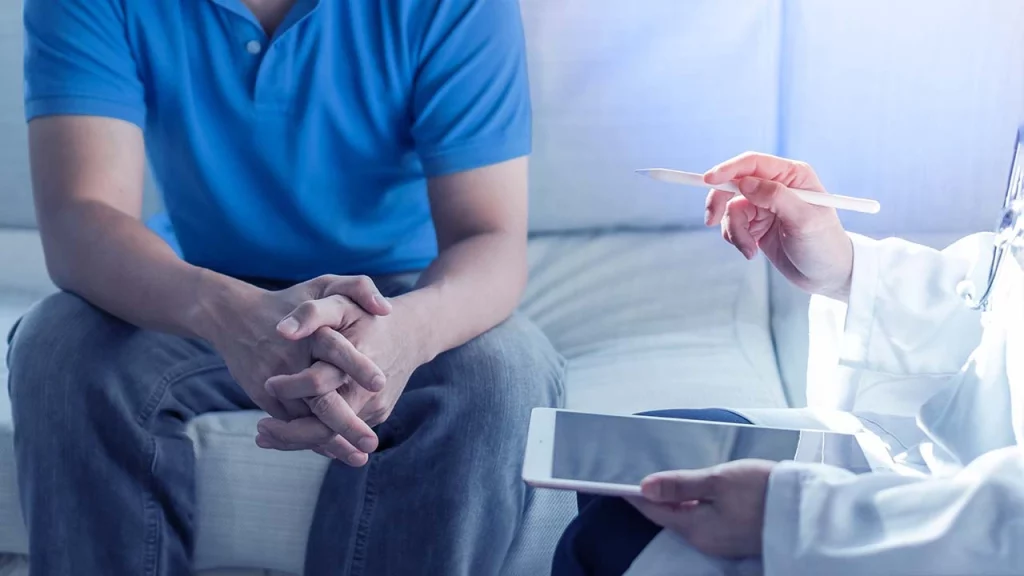 Hombre sentado en una consulta, donde escucha sobre el cáncer de próstata y los síntomas que puede presentar en las diferentes etapas. 
