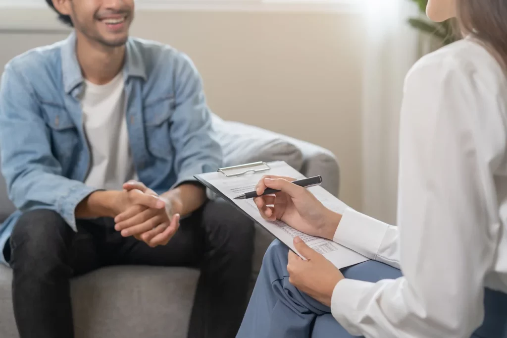 Hombre en consulta de terapia cognitivo conductual, hablando con su psicóloga quien toma notas de la consulta.