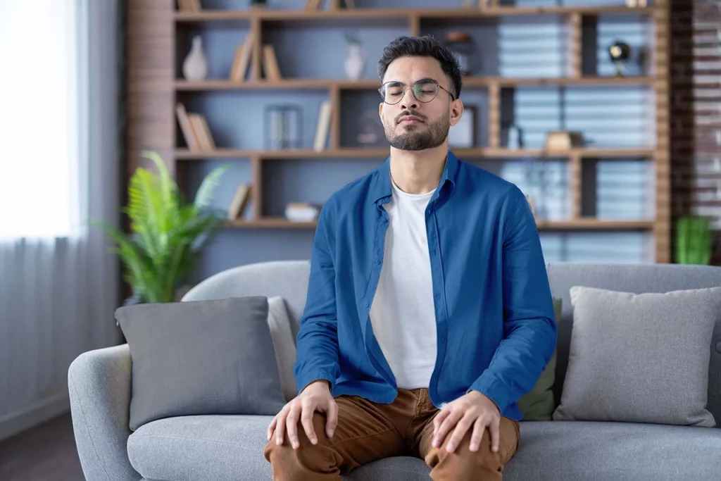 Hombre sentado en un sillón practicando mindfulness, que es una herramienta de meditación para mejorar el bienestar emocional.