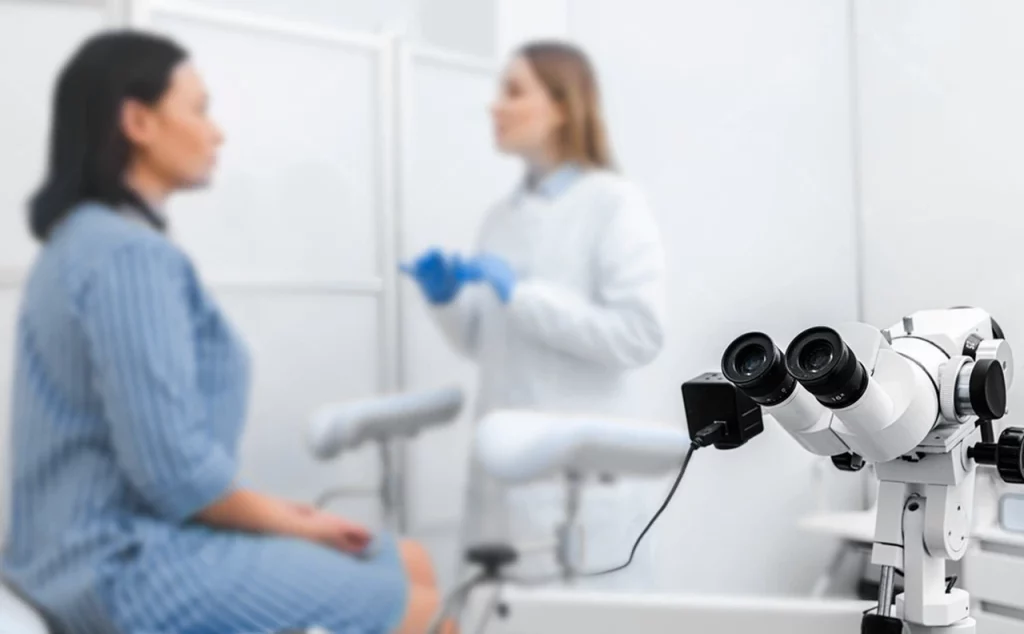 Doctora explicando el procedimiento de colposcopia en el consultorio a su paciente, en primer plano está el colposcopio.